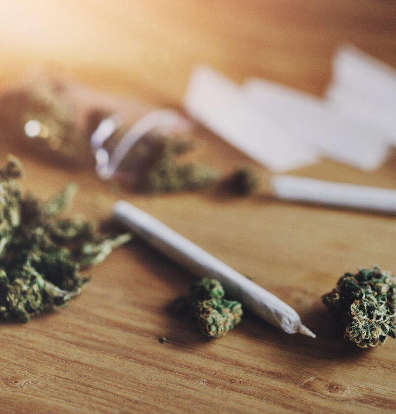 Close-up of cannabis buds, rolled joints, and rolling papers on a wooden surface, with a warm, natural light.